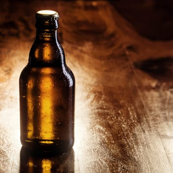 Unlabeled unopened brown bottle of cold beer standing on a wooden bar counter with copyspace for your advertising