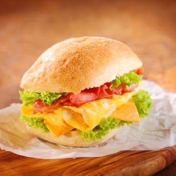 Tasty homemade hamburger filled with slices of pork ham, cheese and green fresh salad or lettuce, served on a paper, on a rustic wooden table