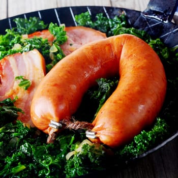 Close up Appetizing Sausage and Smoked Salted Pork on Top of Green Veggies, Served on a Frying Pan.