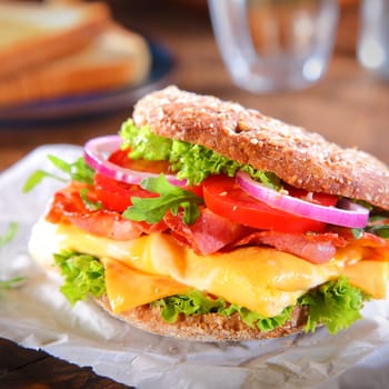Close up Mouth Watering Burger with Bacon, Cheese, Tomatoes, Onions and Lettuce on Top of Burger Paper.
