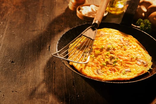 Tasty savory egg omelette with mushrooms and herbs served unfolded in an old frying pan on a wooden table with copyspace