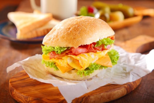 Healthy Fresh Egg Burger with Bacon and Cheese, Added with Lettuce on Top of Wooden Serving Board on Wooden Table.
