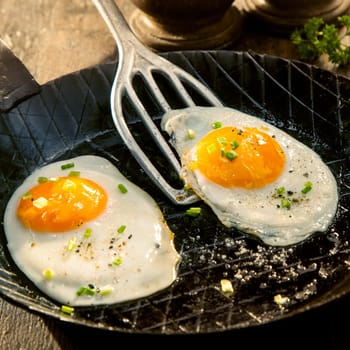 Two fried eggs seasoned with herbs and salt in an old metal pan or griddle ready to be served for a delicious breakfast
