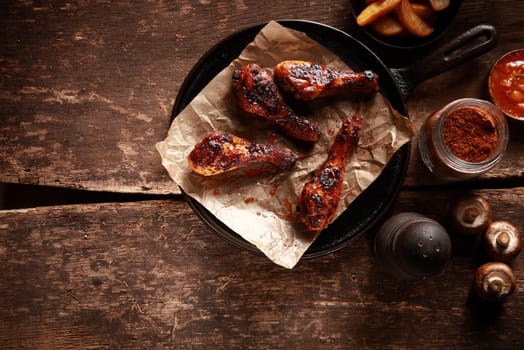 High Angle Looking Down at Saucy Barbecued Chicken Drumsticks on Cast Iron Pan Accompanied by Spices and Ingredients