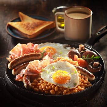 Close up Appetizing Breakfast Meal with Egg, Beans, Sausage,and Bacon on Fan Paired with Bread on Plate with Hot Coffee. Prepared on Wooden Table