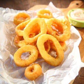 Salty and crispy fried squid rings served on a paper with wasabi mayonnaise, on a wooden cutting board