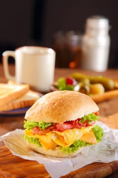Macro Tasty Egg Burger Added with Cheese, Bacon and Lettuce on Burger Paper Place on Top of Wooden Dining Table with Other Dishes.
