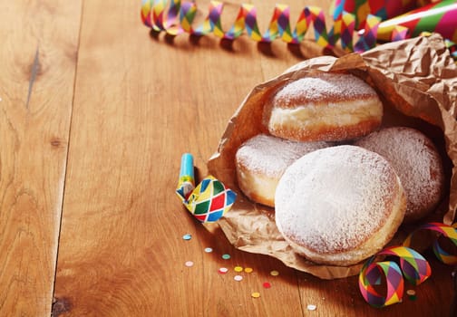 Close up Carnival Donuts with Powdered Sugar on Paper with Colored Props on Sides, Placed on Wooden Table.