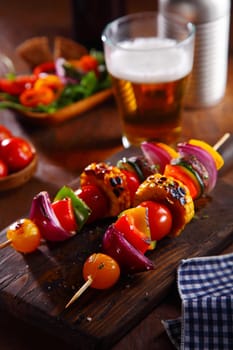 Healthy vegetarian pub lunch with vegan kebabs with a colorful assortment of fresh vegetables roasted on skewers and served with a cold beer and side salad