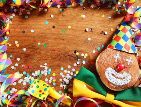 Close up Wooden Table with Colorful Carnival Streamers, Whistle, Confetti, ribbon and Doughnut with Clown Face Design. Emphasizing Copy Space at the Center.