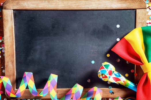 Close up Colorful Carnival Paper Streamers, Whistle and Ribbon in Front Empty Black Board. Emphasizing Copy Space.