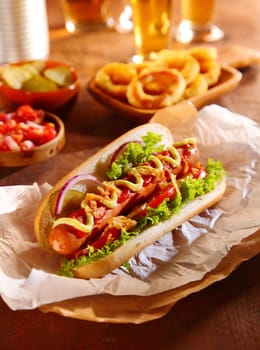Traditional hot dog with a smoked frankfurter on a fresh roll garnished with mustard and ketchup and served with lettuce, tomato and onion