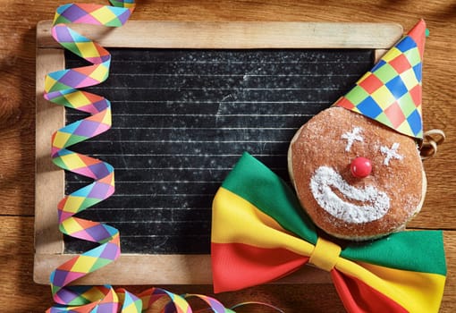Close up Conceptual Carnival Donuts, Decorated with Hat, Ribbon and Confetti, with Black Board at the Back. Placed on Wooden Table. Emphasizing Copy Space for Texts.
