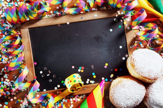 Festival Concept - Close up Empty Black Board Surrounded by Delicious Donuts, Streamers, Confetti, Whistle and Party Cone Hats. Emphasizing Copy Space.