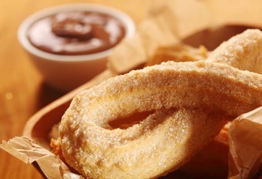 Close up Sweet Churros Snacks in Ribbon Form with Chocolate Dipping Sauce on Side.