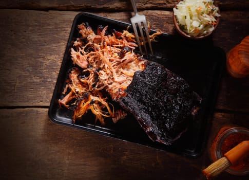 Aerial Shot of Mouth Watering Pulled Pork Dish on Black Serving Tray with Fork. Served on Wooden Table.