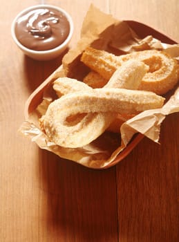 Close up Delicious Churros Snacks on Tray, with Paper, with Chocolate Dipping Sauce on Side. Placed on Wooden Table.