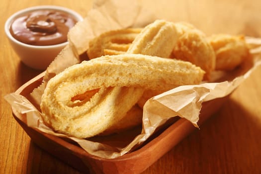 Close up Tasty Churros Snacks on Tray, with Paper, Placed on Wooden Table with Chocolate Dipping Sauce.