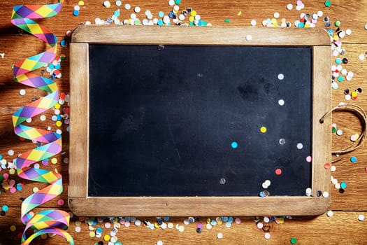 Close up Empty Black Board on Wooden Table with Colorful Streamers and Confetti. Emphasizing Copy Space.