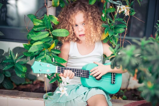 Portrait of a cute girl sitting ouddoor with ukulele