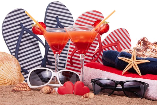 Beach accessories, seashells, sand, two glasses with cocktail and red hearts on white background.  Vacation  in warm countries, beach holiday and party. Honeymoon. Valentine's Day. Romantic travel