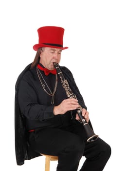 A middle age indigenous man playing his clarinet in a black outfit and.red hat and bow, isolated for white background.