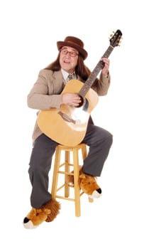 A middle age indigenous man in fancy shoes sitting and playing.his guitar in a jacket and hat, isolated for white background.