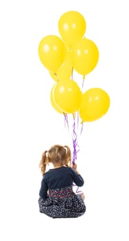 portrait of a sitting 3 year old girl holding a group of yellow balloons. seen from behind. isolated on white