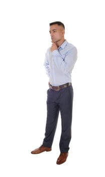 A handsome young east Indian man standing in a blue shirt with his.one hand under his chin, thinking, isolated for white background.