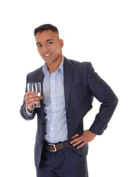 A young east Indian man standing in his suit with a glass of water, .looking into the camera and drinking, isolated for white background.