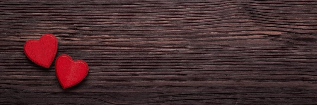 Two decorative hearts on dark brown wooden background. Top view with copy space. Valentine's Day. Design element for romantic greeting card, wedding invitation. Extra wide panorama banner background