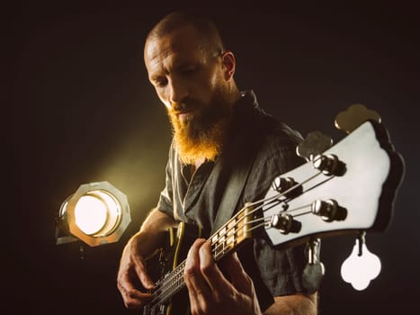Photo of a bearded man playing bass guitar on stage in front of spotlights..