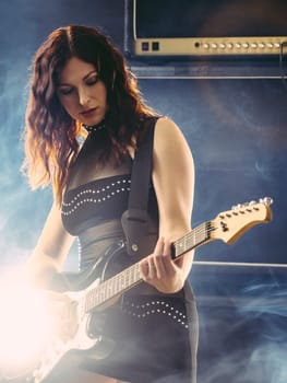 Young beautiful redhead woman playing an electric guitar in front of large amplifier.