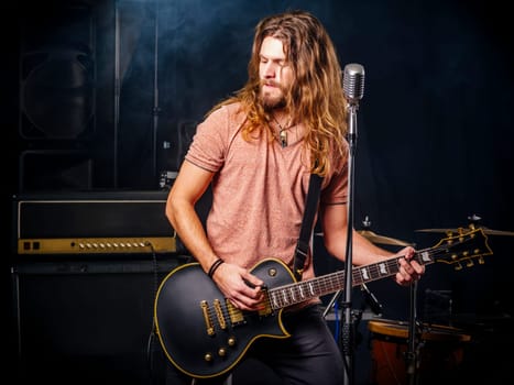 Photo of a young man with long hair and beard playing electric guitar on stage.
