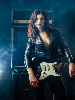 Young beautiful redhead woman playing an electric guitar in front of large amplifier.