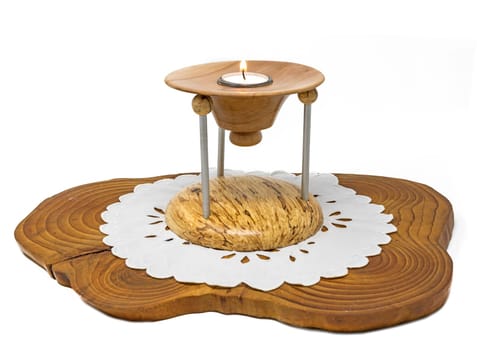 Multi-part wooden candlestick with burning candle stands on a dark wooden board isolated on white