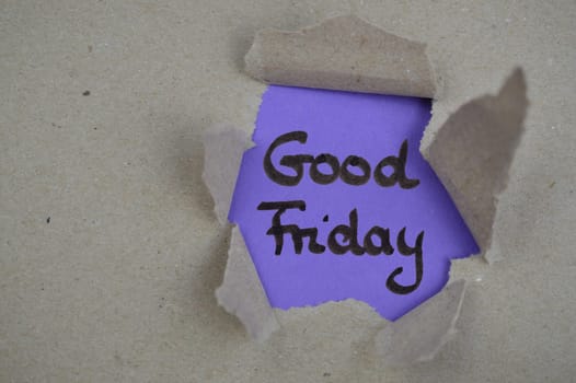 The words Good Friday on purple paper beneath ripped open gray packing paper visible through a hole