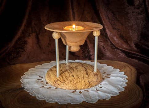Multi-part wooden candlestick with burning candle stands on a dark wooden board against brown background