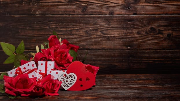 Bouquet of red roses, decorative hearts and gift boxes on dark brown wooden background with copy space. Valentine's Day. Wedding Day. Design element for romantic greeting card and invitation