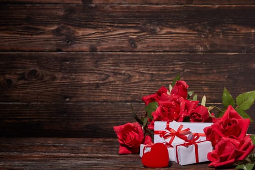 Bouquet of red roses, decorative hearts and gift boxes on dark brown wooden background with copy space. Valentine's Day. Wedding Day. Design element for romantic greeting card and invitation