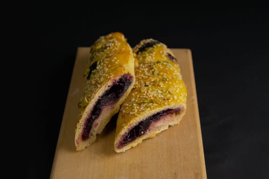 Freshly prepared puff pastry with cherry and sesame seeds close-up in a black background. Details The concept of home baking, breakfast, snack.