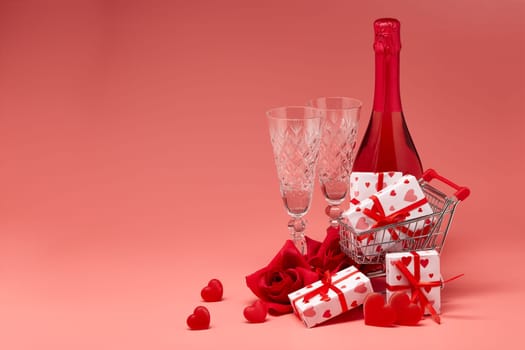Shopping trolley, gift boxes, red roses and hearts, champagne and flutes on pink background with copy space. Valentine's Day. Festive background with decorative hearts.Valentine's Day. Wedding day.