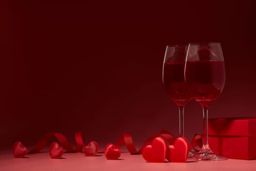 Gift box, red hearts, two glasses with wine on red background. Valentine's Day card. Copy space. Design element for romantic greeting card, wedding invitation.