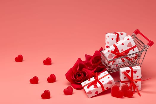 Shopping trolley with gift boxes, red roses and hearts on pink background with copy space. Festive background with decorative hearts.Valentine's Day. Wedding day.