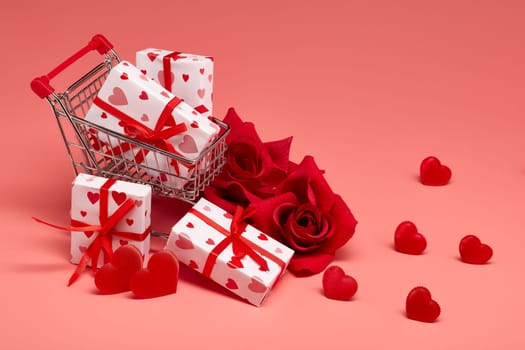 Shopping trolley with gift boxes, red roses and hearts on pink background with copy space. Festive background with decorative hearts.Valentine's Day. Wedding day.