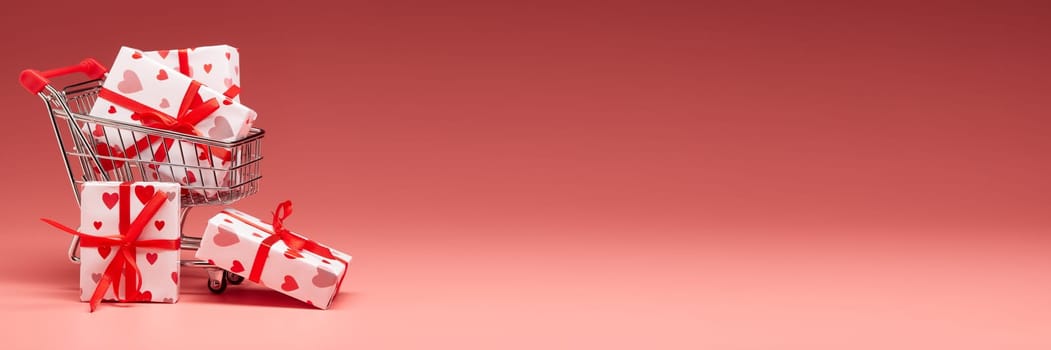 Shopping trolley with gift boxes on pink background with copy space. Valentine's Day. Mother's day, wedding, women's day. Extra wide panorama banner background