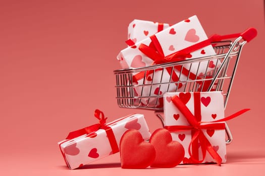 Shopping trolley with gift boxes and red hearts on pink background. Festive background with decorative hearts.Valentine's Day. Wedding day.