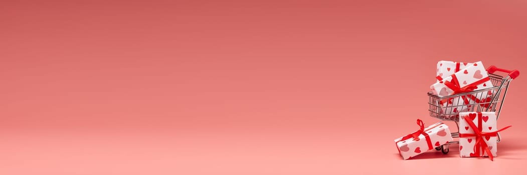 Shopping trolley with gift boxes on pink background with copy space. Valentine's Day. Mother's day, wedding, women's day. Extra wide panorama banner background