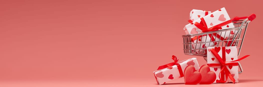 Shopping trolley with gift boxes and red hearts on pink background with copy space. Valentine's Day. Wedding day. Extra wide panorama banner background