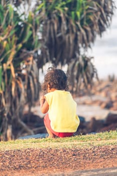 Back view of little cute bare feet kid boy sitting alone in the countryside park road in summer time. Sunset sunlight. Happy Childhood Outdoors and lifestyle concept. Copy Space for text.